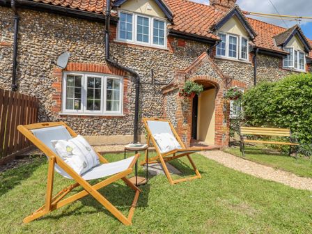 A stone cottage exterior with two wooden lounge chairs on a lawn and a wooden bench nearby at Bluebird Cottage in Newmarket