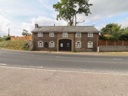 A stone house with white framed windows and a large wooden door facing a road at The Old Custom House in Wangford