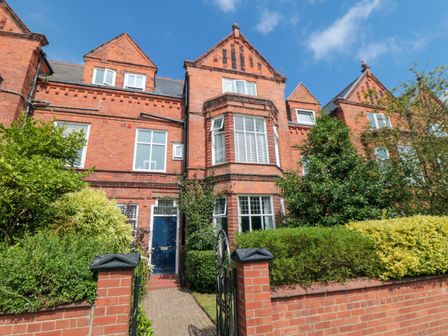 A brick townhouse with a blue door surrounded by greenery and a small brick wall in front at South Bay House in Scarborough