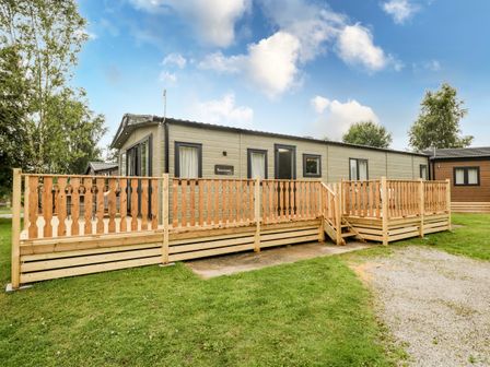 A mobile home with wooden decking and railing on a grassy plot at Ashton Lodge - Sherwood 4 in South Lakeland Leisure Village