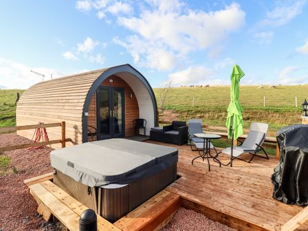 An outdoor wooden deck with a hot tub chairs table umbrella and a wooden pod at Gander Pod Near Clifton Upon Teme