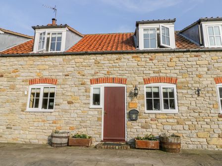 Stone exterior of a cottage with a red door four white windows and flower pots at Barn Cottage Marton near Kirkbymoorside