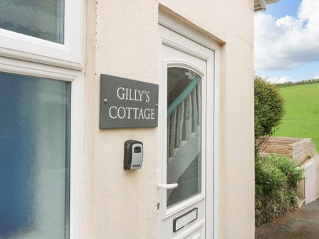A white front door with a glass panel and a sign that reads Gilly's Cottage on the wall beside it at Gilly's Cottage in Hope Cove