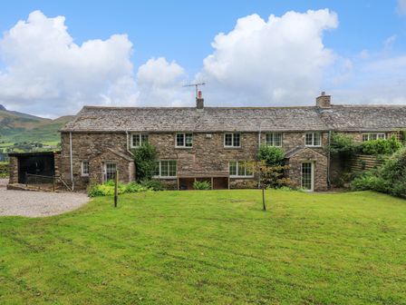 A stone house with grass lawn and cloudy sky at Flaska House in Troutbeck Near Penrith