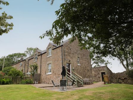 A stone cottage with outdoor seating and a garden at 1 Roddam Rigg Cottage in Roddam near Wooler