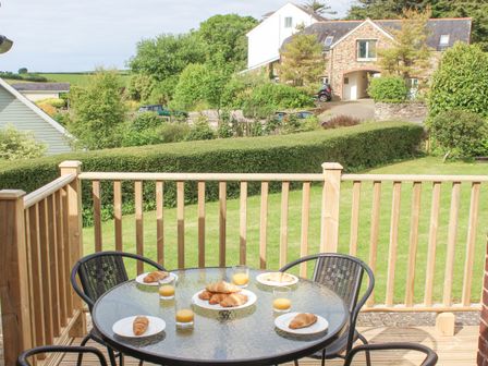 A patio table with croissants and glasses of orange juice on a balcony overlooking a garden and houses at 5 Keeper's Cottage Hillfield Dartmouth