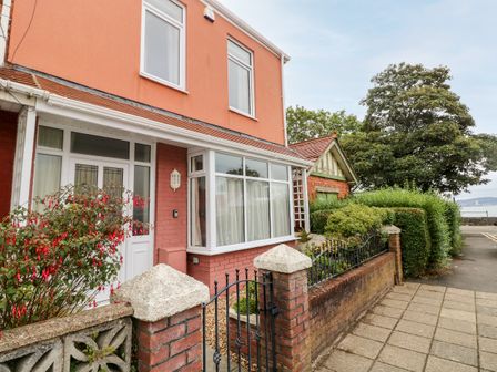 Exterior view of a house with a red brick wall gate and flowering shrub at The Headlands - Gower in The Mumbles