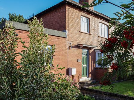 A two story brick house with a green door and garden plants at The Firs in Scalby