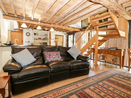 A living room with a black leather sofa and wooden staircase at Tinkley Cottage in Nympsfield near Nailsworth