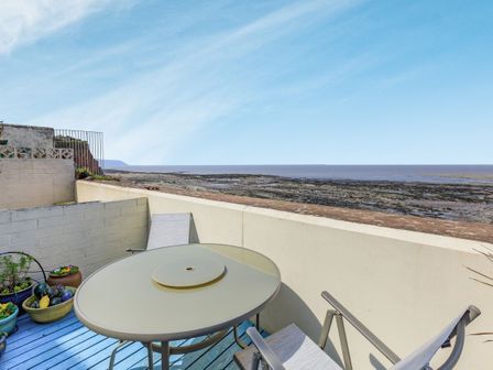 An outdoor patio with a round table and chairs overlooking a rocky coastline at Sea Spray in Watchet
