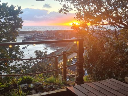 A coastal view at sunset with buildings near water and string lights on a wooden railing at Windycroft in Barmouth