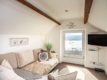A small living room with a beige sofa and a window overlooking boats on the water at Arran House in Barmouth