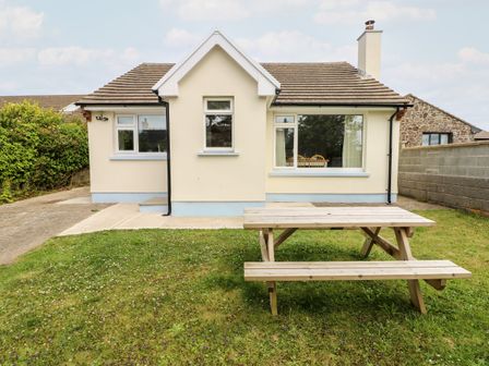 A backyard with a wooden picnic table and a cream colored house with multiple windows at Chalfonts Cottage in Trefin near Penparc