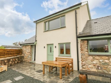 An outdoor patio area with a wooden table and bench set outside a stone and plaster house at Ty Gwair The Hayloft in Caernarfon