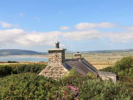 A stone cottage roof with chimneys surrounded by bushes and overlooking a coastal landscape at Sunstone Garreg Haul in Cilan near Abersoch