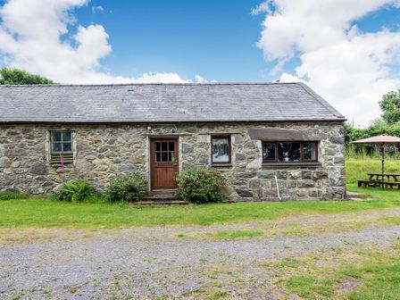 A stone cottage with a wooden door and three windows with a picnic table and umbrella on the side at Tryfan Cottage in Rhostryfan near Caernarfon