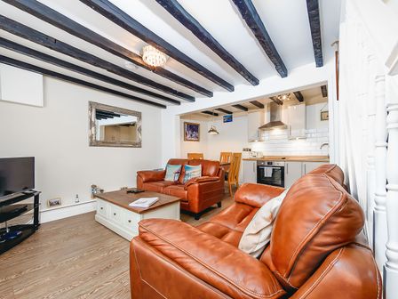 A living room with brown leather sofas a wooden coffee table a wall mirror a television and an open kitchen with dining table at 5 Ivy Yard in Whitby