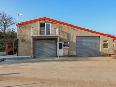 A commercial building with two large metal roller doors and a small balcony above one door at The Apartment at Plas Yr Eithin in Amlwch near Llanfechell