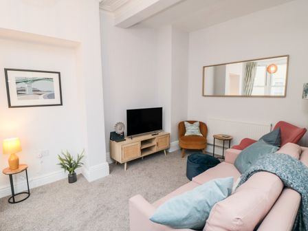 A living room with a pink sofa and brown chair with a television on a wooden stand at 1 Princess Street in Scarborough