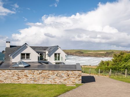A coastal house with a stone wall and a driveway overlooking the sea at Seascape in Polzeath