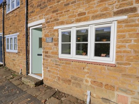 The exterior of a stone cottage with a green door and white framed windows at Bumble Cottage in Tysoe