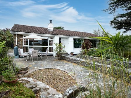 An exterior view of a bungalow with a stone patio table and chairs and plants at Longhouse Bungalow in Rock
