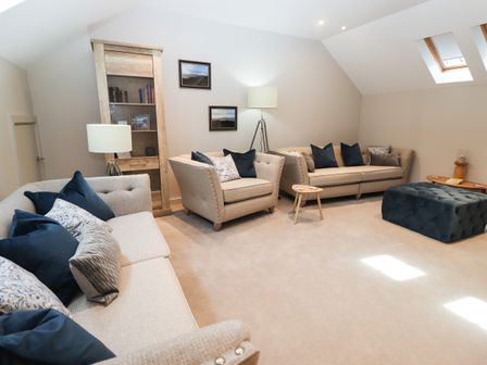 A living room with beige sofas and blue pillows a wooden cabinet and a blue ottoman at 21 Ironworks in Ulverston