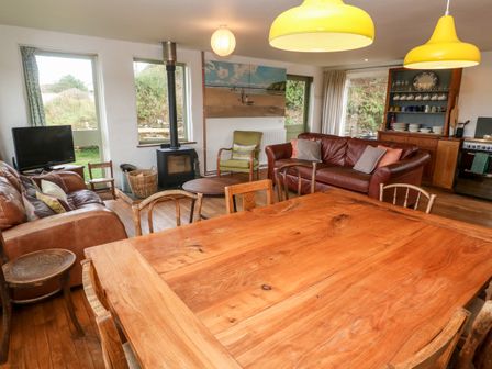 A living room with wooden dining table chairs two brown leather sofas wood burning stove and kitchen area at Porth Farm Annexe in Mawgan Porth