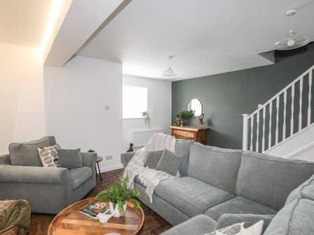 A living room with gray sofas a wooden chest a round wooden coffee table and a staircase at Y Goedwig in Newborough