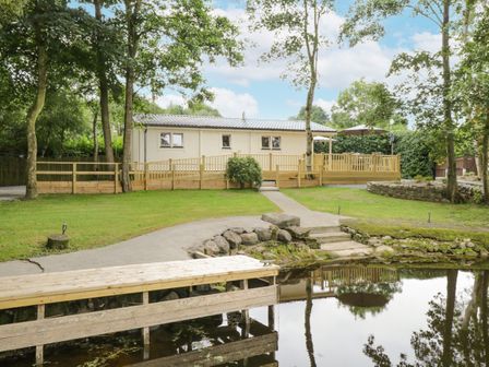 A wooden cabin with a deck and outdoor furniture by a pond with trees surrounding it at Port Heron Lodge Ballykeeran near Glasson County Westmeath
