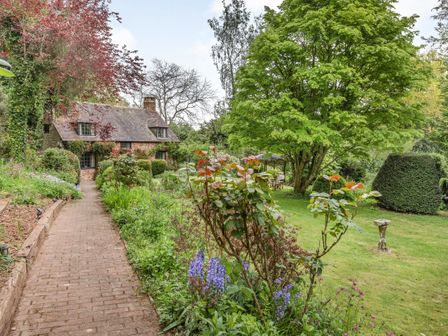 A garden path with flowers and bushes leading to a stone house with a chimney and slate roof at Saint Pancras Chapel in Washford near Williton