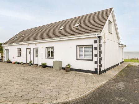 Exterior of a white house with a brown tiled roof and several windows and doors with potted plants outside at Curragh Hill in Mulranny County Mayo
