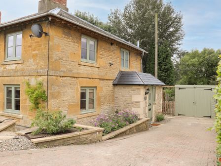 Stone house with green framed windows driveway flower bed and green garage doors at 4 Lower Folley in Chipping Campden