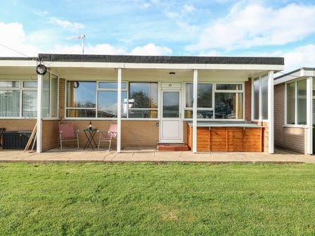 A patio area with two folding chairs a small table and a wooden storage box outside a single story house at 31 Seaward Crest in Mundesley