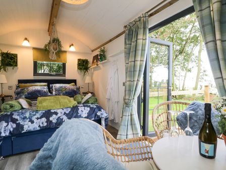 A bedroom with a double bed and floral bedding next to a table with two chairs by a glass door at High Rigg Shepherd's Sunset in Brampton Cumbria