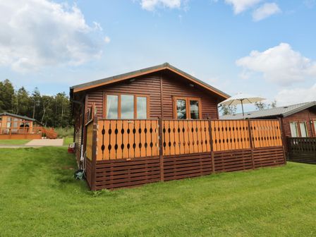 A wooden cabin with a fenced deck and umbrella on grass at Hillside View in Alnwick