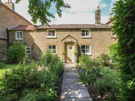 A stone cottage with a garden path leading to a central door surrounded by plants and shrubs at Black Horse Cottage in Swainby