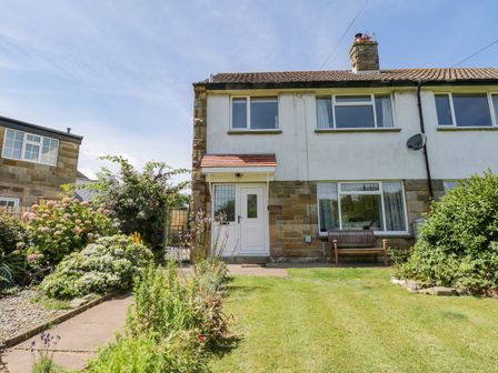A garden with plants flowers and a bench in front of a semi detached house at Sea Change in Newholm near Whitby