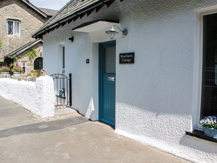 The entrance of a white cottage with a blue door and a black sign reading Moorhurst Cottage in Kents Bank near Grange Over Sands