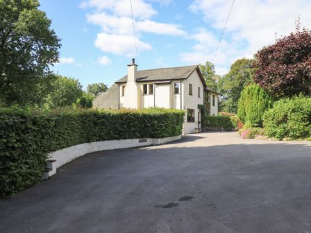 A driveway leading to a two-story white house surrounded by hedges and trees at Greenbank Cottage in Winster near Bowness-On-Windermere