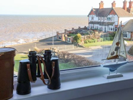 A window view with binoculars and a decorative sailboat on the sill overlooking a road and the sea at Sea Spell Loft in Hornsea