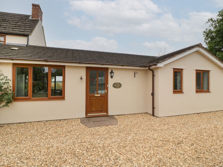 Exterior view of a single-story house with a gravel driveway and windows at The Honey Pot in Stroat near Chepstow