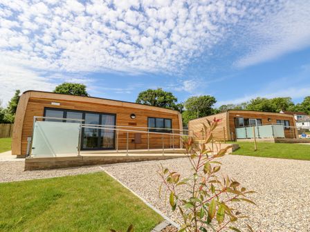 Two wooden modern cabins with glass railings on a gravel and grass lawn under a partly cloudy sky at Barolo in Seaview