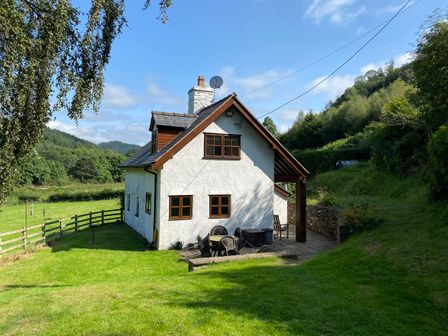 A white cottage with wooden window frames surrounded by grass and trees at Tan Y Garth Cottage in Glyndyfrdwy near Llangollen