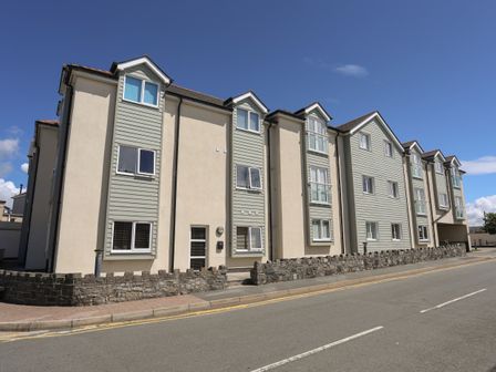 A multi-story residential building with beige and light green siding along a street at 8 Pen Llanw Tides Reach in Rhosneigr