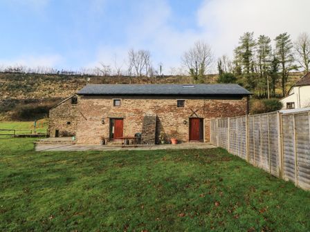 A stone cottage with two wooden doors and a skylight surrounded by grass and fencing at Red Deer Cottage in Wheddon Cross