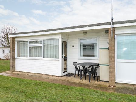 A patio with a round table and three chairs outside a white building at Chalet 12 in Hemsby