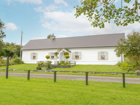 A white cottage with gray roof and shuttered windows on a grassy lawn at Lakeside Cottage in Cavetown near Boyle County Roscommon