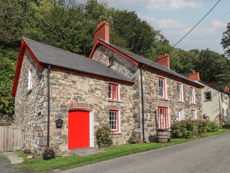 Stone cottage with red door and window frames along a road bordered by greenery at Sycamore Vestry in Pontfaen near Fishguard