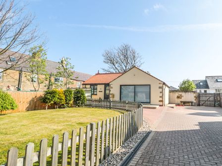 A fenced lawn garden and a small cream house with a red tiled roof at 3 The Paddock in Benthall near Beadnell